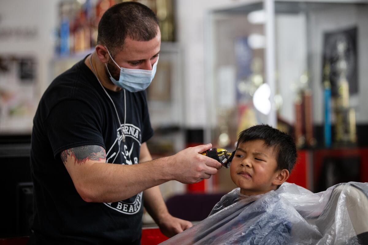 Zach Devela, 3, gets his hair cut by barber student Bassam Tominah.