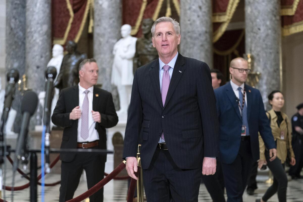 McCarthy, wearing a dark suit, white shirt and pink tie, is walking in the Capitol's Statuary Hall        