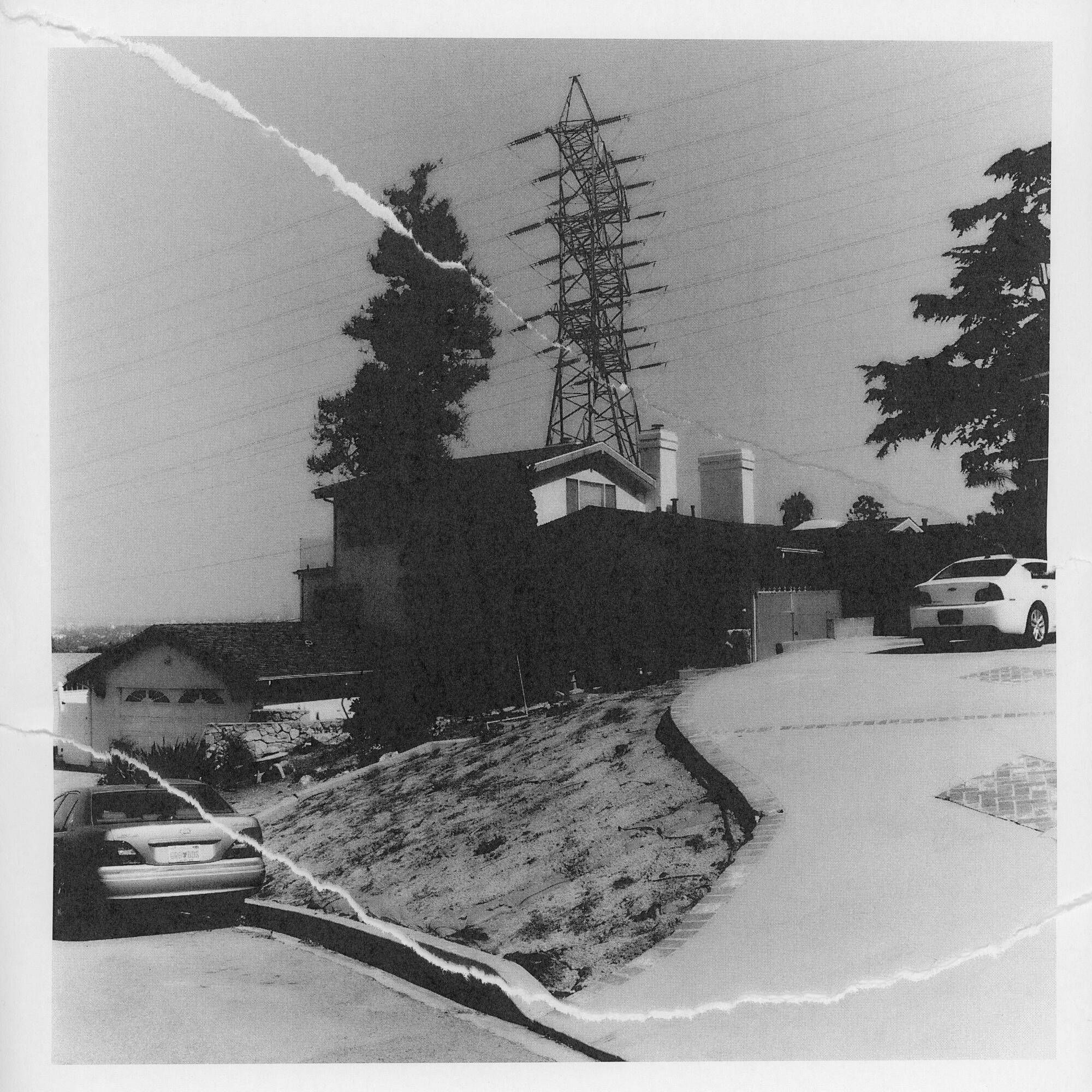 A ripped, black-and-white photo of a driveway and house in the distance.