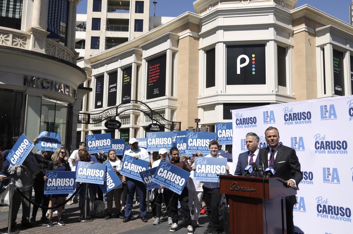 Rick Caruso and Joe Buscaino surrounded by Rick Caruso signs at the Grove.