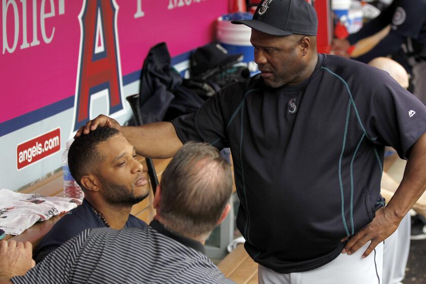 Seattle Mariners’ Robinson Cano is examined by Manager Lloyd McClendon, right, and trainer Rob Nodine, after a ball hit his forehead on an overthrow by Angels shortstop Taylor Featherston between innings on Saturday.