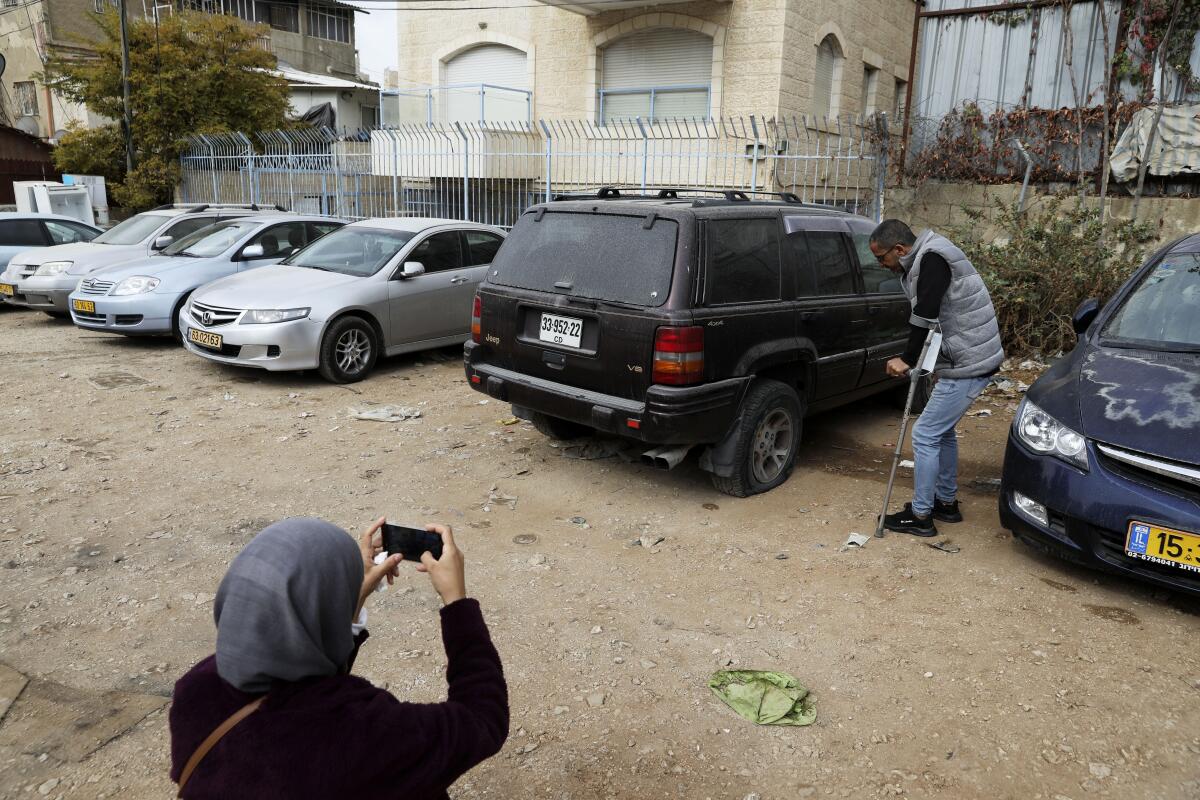 A woman photographs a vandalized vehicle in the Sheikh Jarrah neighborhood of east Jerusalem