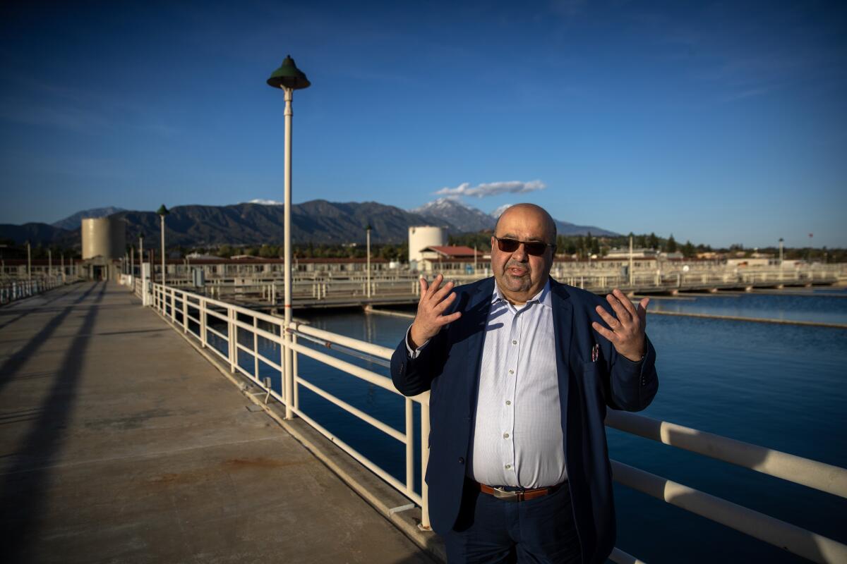 A man gestures with his hands while speaking in front of a wastewater treatment plant.