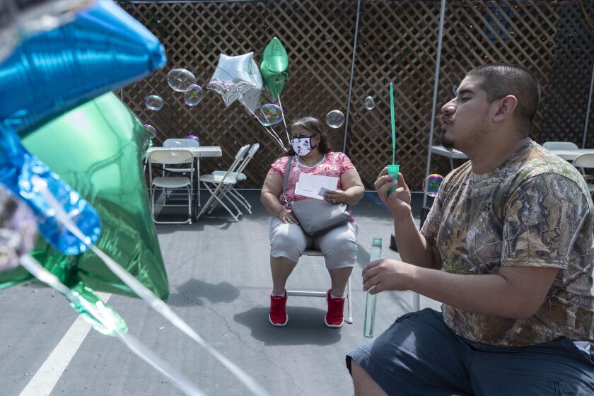 REDONDO BEACH, CA - APRIL 11: Daniel Arana, 20, blows soap bubbles in the post-shot waiting area with his mother Yolanda following his mock vaccination on Sunday, April 11, 2021 at Friendship Foundation in Redondo Beach, CA. The mock clinic is being held at the Friendship Foundation through Disability Voices United in Redondo Beach for individuals with intellectual disabilities. Real nurses will use syringes without the needle in an environment meant to mimic a vaccine site to help prepare vulnerable people for the vaccine, which they'll get in a few weeks. The event will be used to train Curative staff. (Myung J. Chun / Los Angeles Times)