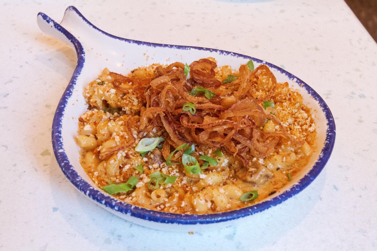 A circular ceramic baking dish filled with pimento mac ’n’ cheese with smoked brisket, topped with fried onions