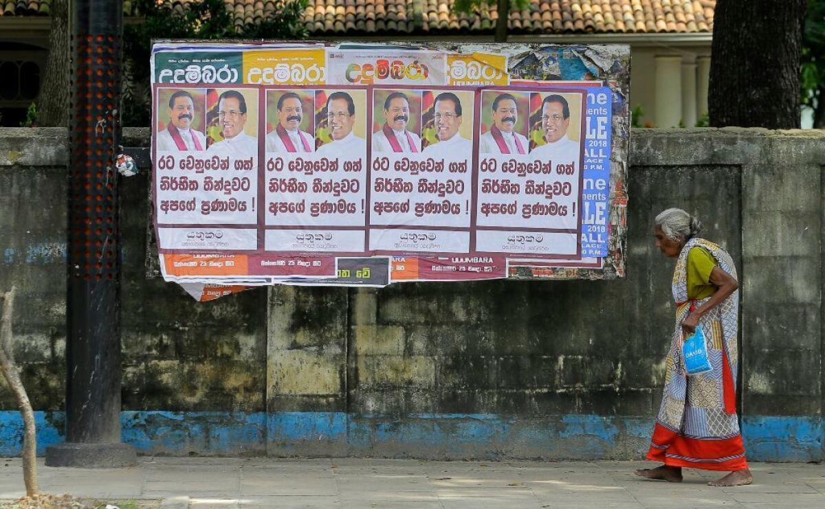 A Sri Lankan woman walks past a notice board covered with posters carrying portraits of President Maithripala Sirisena and newly appointed Prime Minister Mahinda Rajapaksa on a street in Colombo, Sri Lanka, on Sunday.