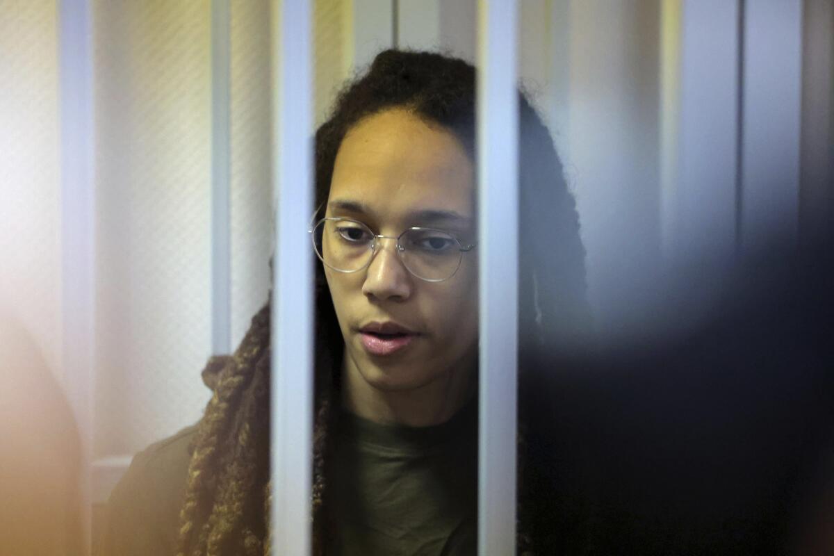 WNBA star and two-time Olympic gold medalist Brittney Griner stands behind bars in a courtroom for a hearing.