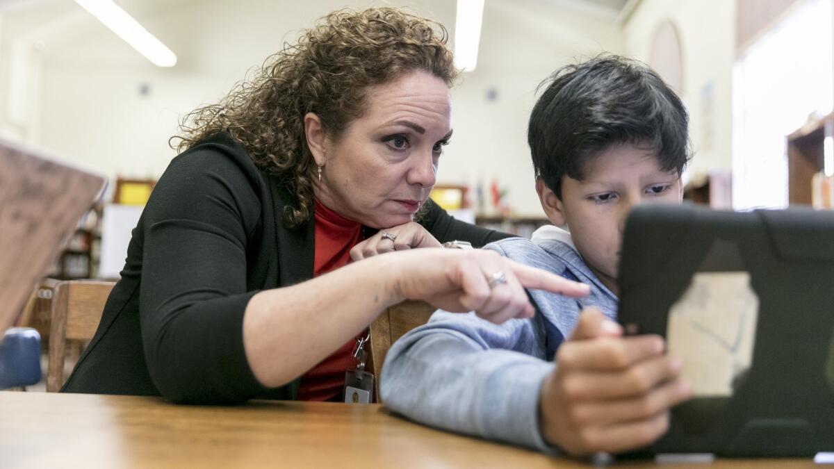 Maria Magnanimo-Toledo, an administrative specialist at the L.A. Unified School District but serving as a substitute teacher, works wit Isaiah Ganboa, 11, while she leads a sixth-grade math class at the library of El Sereno Middle School.