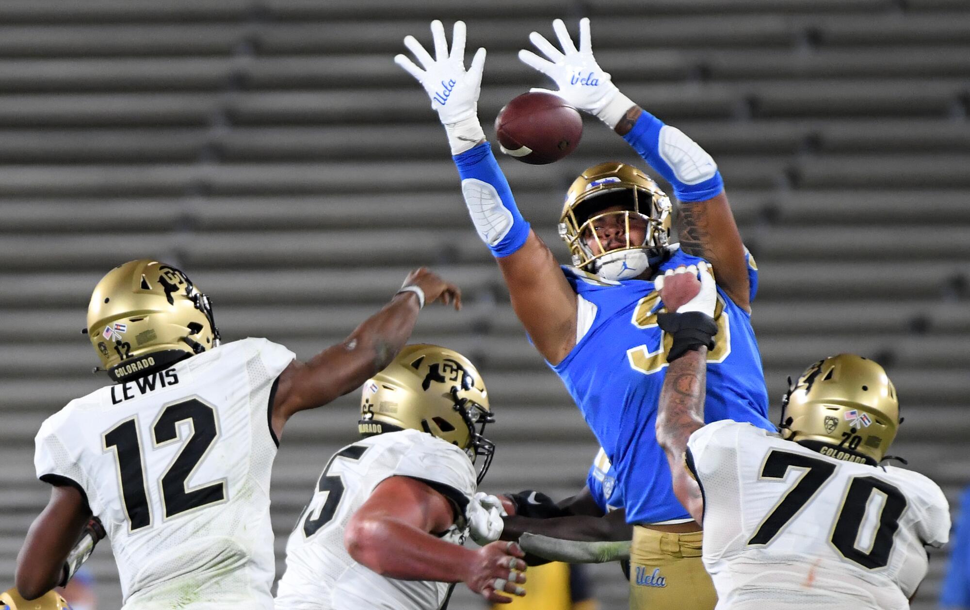 : UCLA defensive lineman knocks down a pass from Colorado quarterback.