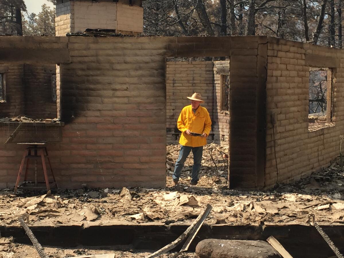 In this photo provided by Rusty Bowers, Arizona House Speaker Rusty Bowers walks through the remains of his family's weekend home on Tuesday, June 8, 2021, that was destroyed by a wildfire the day before. Bowers used the home in the remote mountains as a family retreat and often did his artwork there. (Elijah Cardon/Rusty Bowers via AP)