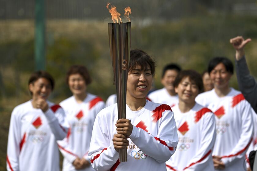Japanese torchbearer Azusa Iwashimizu, center, a member of Japan women's national football team, arrives at a torch kiss point to pass on the flame during the torch relay grand start outside J-Village National Training Center in Naraha, Fukushima prefecture, northeastern Japan, Thursday, March 25, 2021. The torch relay for the postponed Tokyo Olympics began its 121-day journey across Japan on Thursday and is headed toward the opening ceremony in Tokyo on July 23. (Philip Fong/Pool Photo via AP)