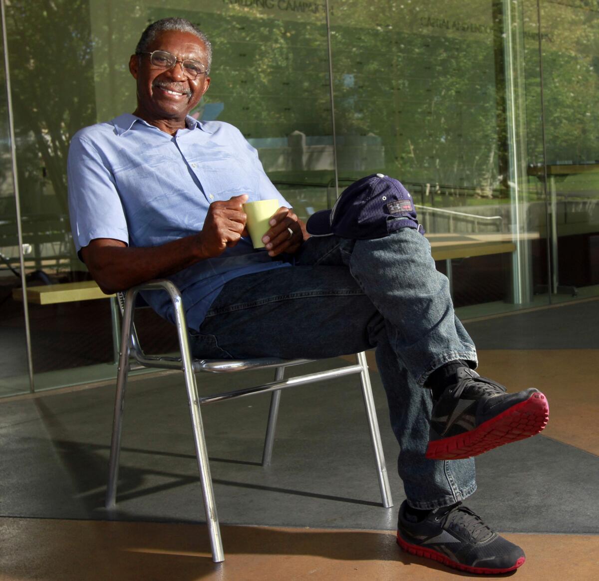 Holding a coffee cup, Charlie Robinson smiles as he leans back in a chair with his legs crossed.