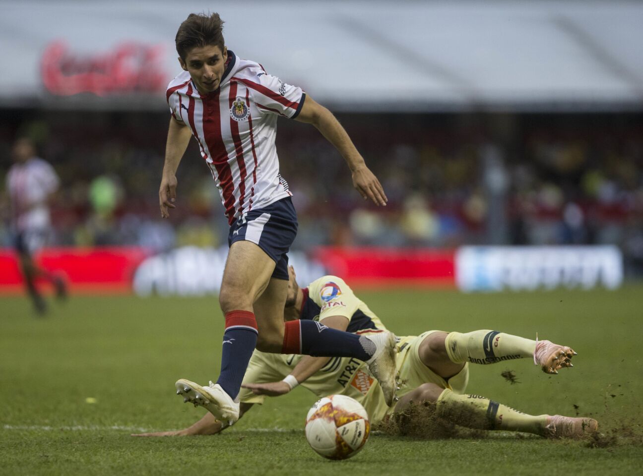 Chivas' Isaac Brizuela falls as he fights for the ball with America's Matheus Uribe during a local soccer league match in Mexico City, Sunday, Sept. 30, 2018.
