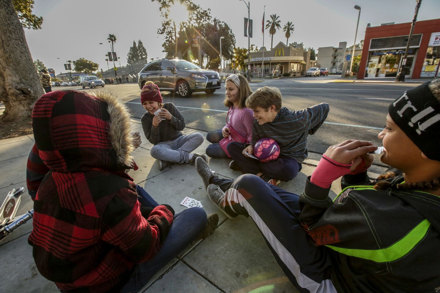 Christianna Watkins, 12, right, from Lake Elsinore, and her friends play a card game sitting along Colorado Boulevard in advance of Friday's parade.