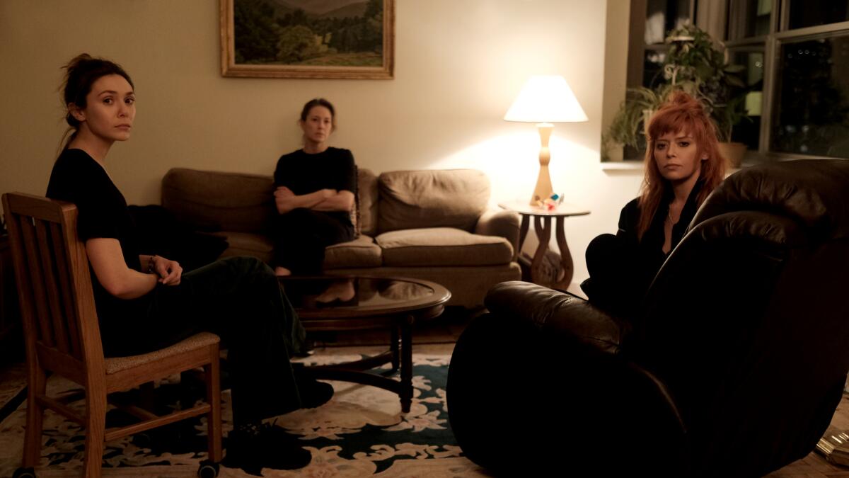 Three women sit pensively in a living room.