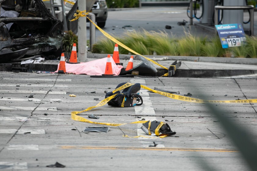 A body covered by a sheet lies in the street next to debris and the burned wreckage of a vehicle