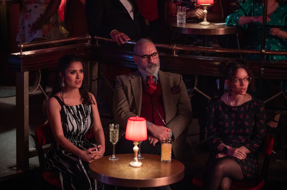 A man sits between two women at a small table in the audience of a theater