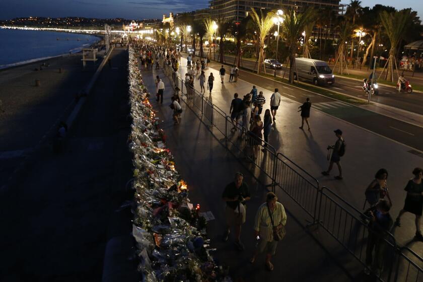 People walk on the Promenade des Anglais in Nice, France, on July 20, 2016, next to floral tributes, notes and candles placed in the road for victims of the deadly Bastille Day attack.