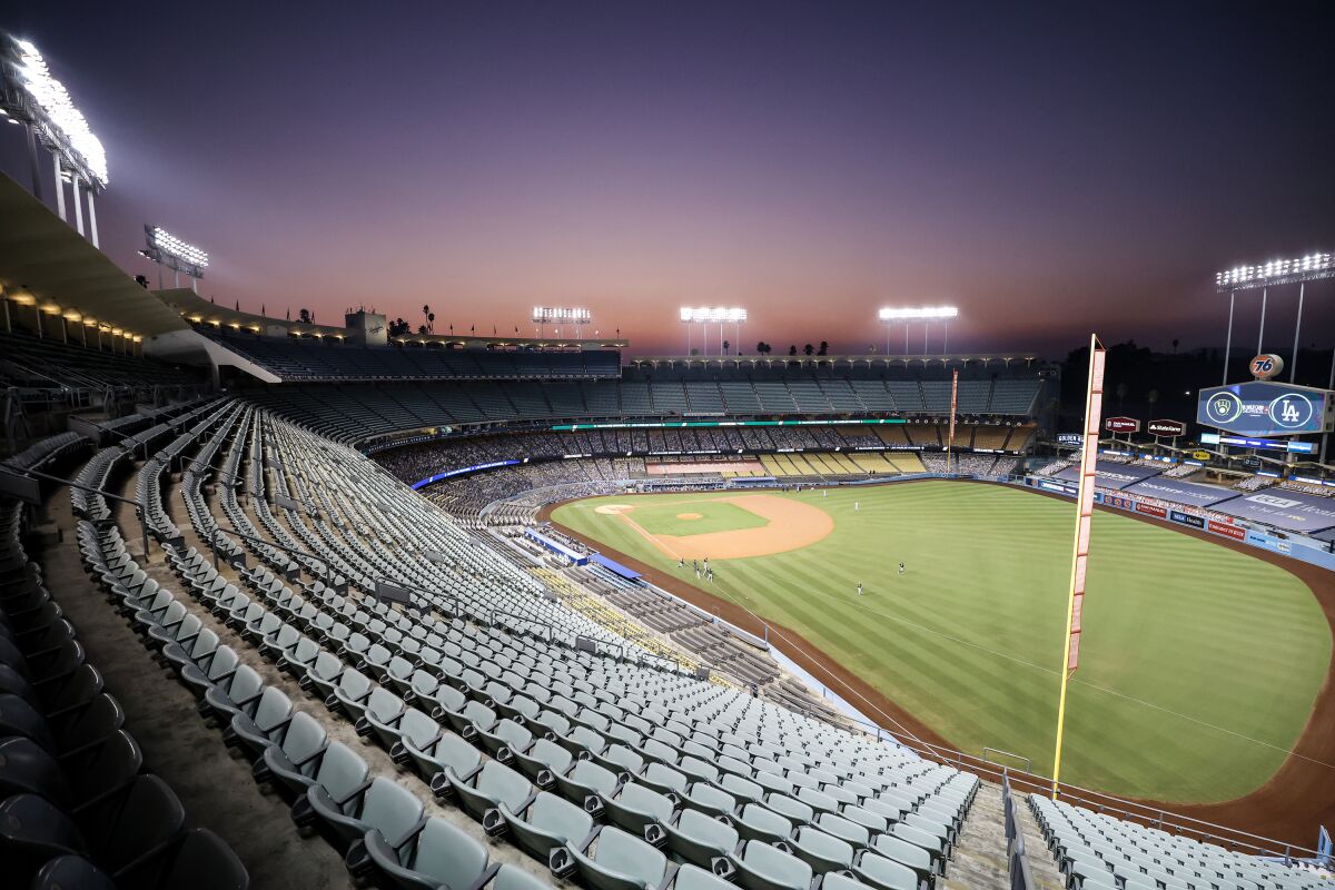 An empty Dodger Stadium at dusk, with players on the field in the distance