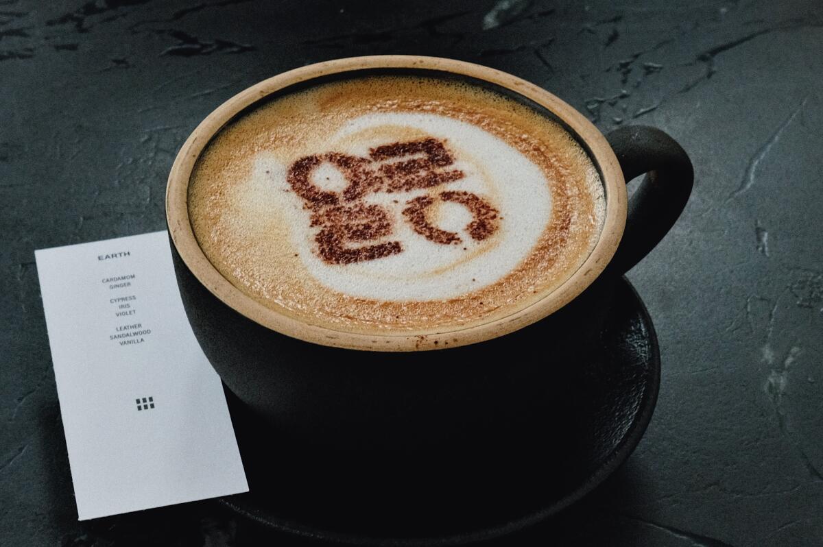 A coffee cup topped with latte art on a counter at Elorea in Koreatown. Beside it, a slip of paper fragrance card.