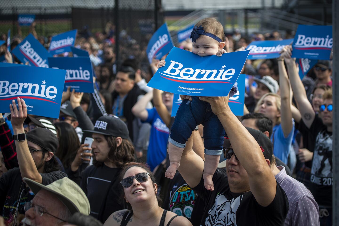 SANTA ANA, CALIF. -- FRIDAY, FEBRUARY 21, 2020: David Reyes holds up his baby, Galadriel Reyes, 8 months old, as his wife, Erica Smith watches and joins supporters cheering as they listen to U.S. Senator and Democratic Presidential candidate Bernie Sanders speak at Valley High School in Santa Ana, Calif., on Feb. 21, 2020. (Allen J. Schaben / Los Angeles Times)