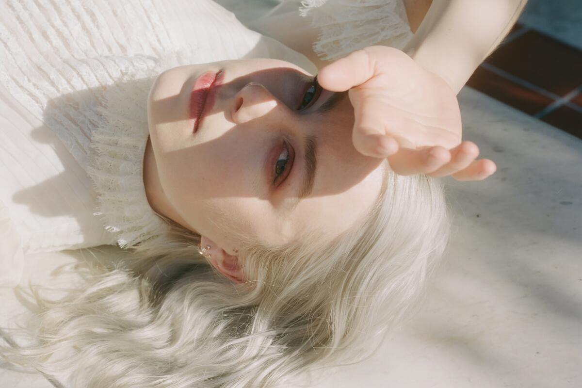 Phoebe Bridgers lays down in a white dress and shields her eyes from the sun.