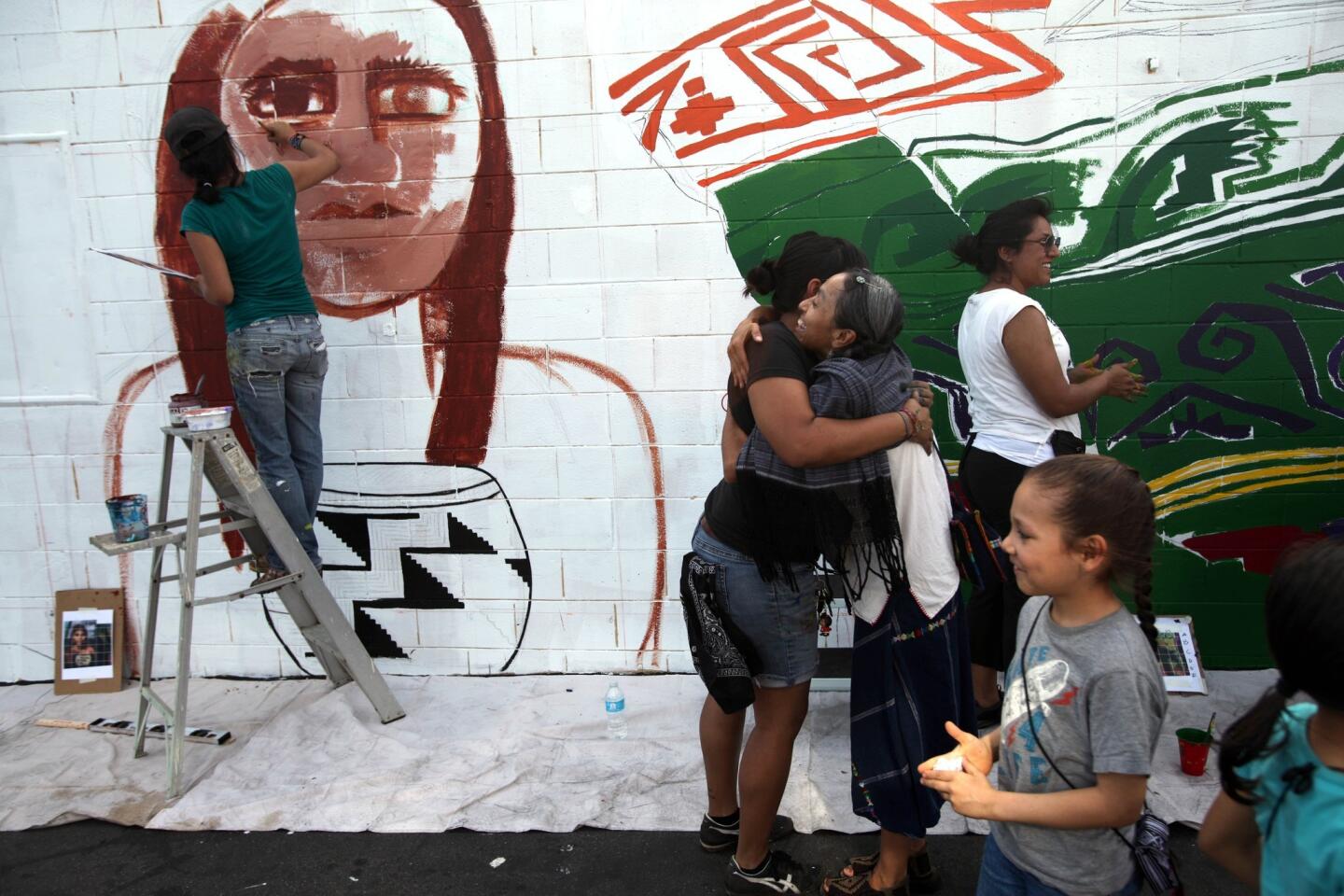 Meztli Icue Papalotl gets a hug after her three daughters helped start a mural being painted by the HOODsisters collective in Pacoima.