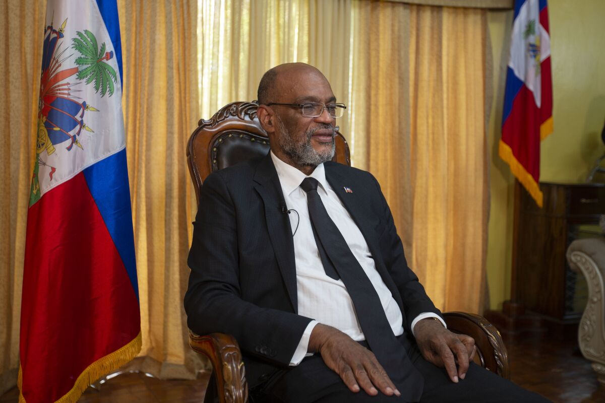 Haiti's Prime Minister Ariel Henry sits between two flags in front of drapes.