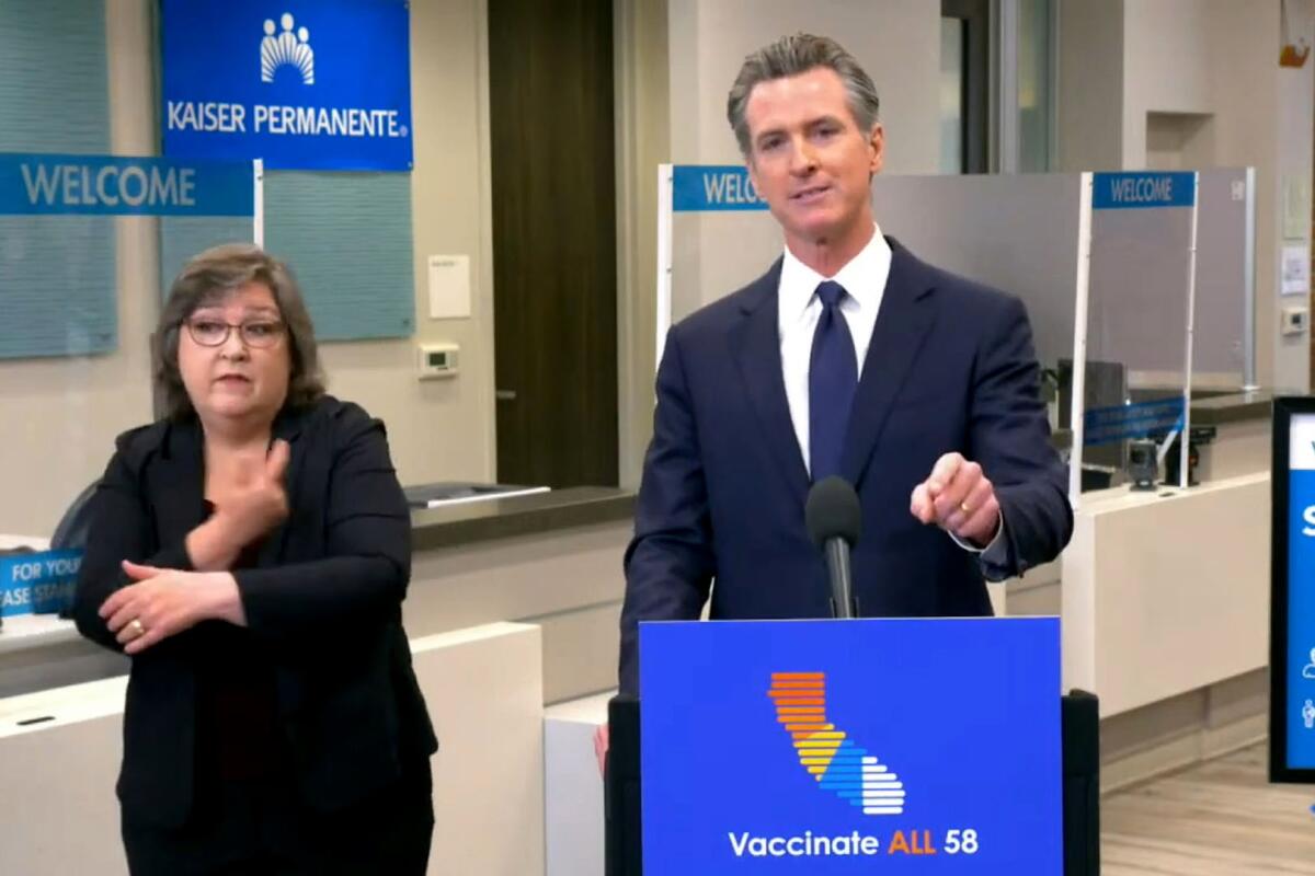 Gavin Newsom stands at a podium. At his side is a sign language interpreter.