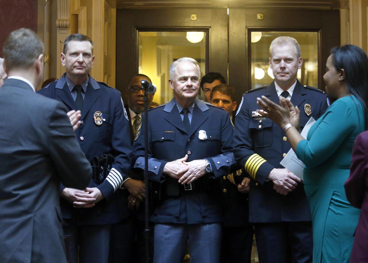 Three men in police uniforms stand facing two people on the sides who are applauding