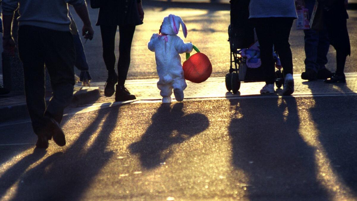 A girl in a bunny costume crosses a street with her parents as the sun sets.
