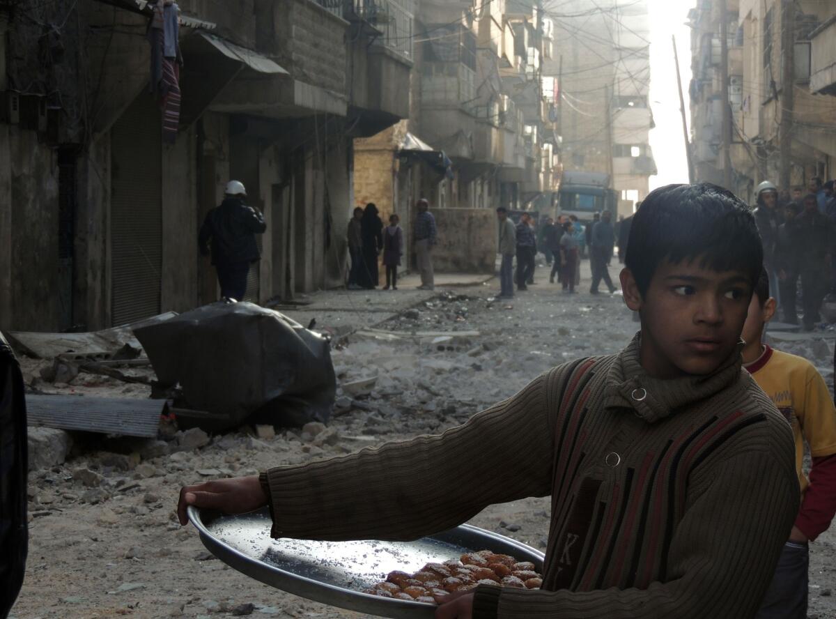 A Syrian boy sells sweets as civilians and emergency personnel inspect the damage in a street after government forces allegedly shelled the northern city of Aleppo.