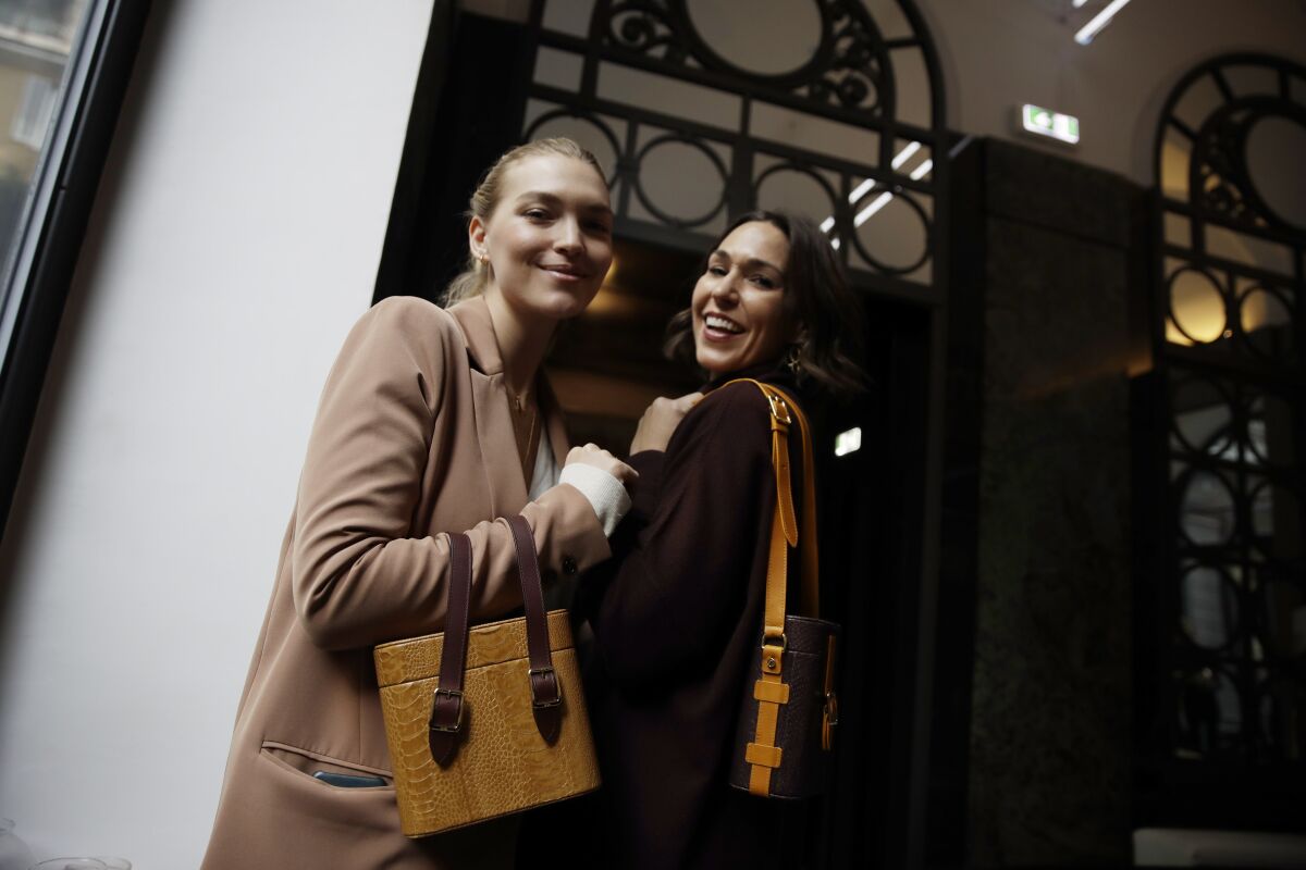 FILE - In this Feb. 24, 2019 file photo, model Arizona Muse, left, is flanked by designer and Officina del Poggio owner Allison Hoeltzel Savini as they present a creation of the Officina del Poggio women's Fall-Winter 2019-2020 collection, in Milan, Italy. The United States’ fumbling response to the pandemic is casting doubt on its economic prospects and making it one of the chief risks that could undermine the rebound. Officina del Poggio sells 60% its vintage motorcycle-inspired satchels to U.S. customers. (AP Photo/Luca Bruno, file)
