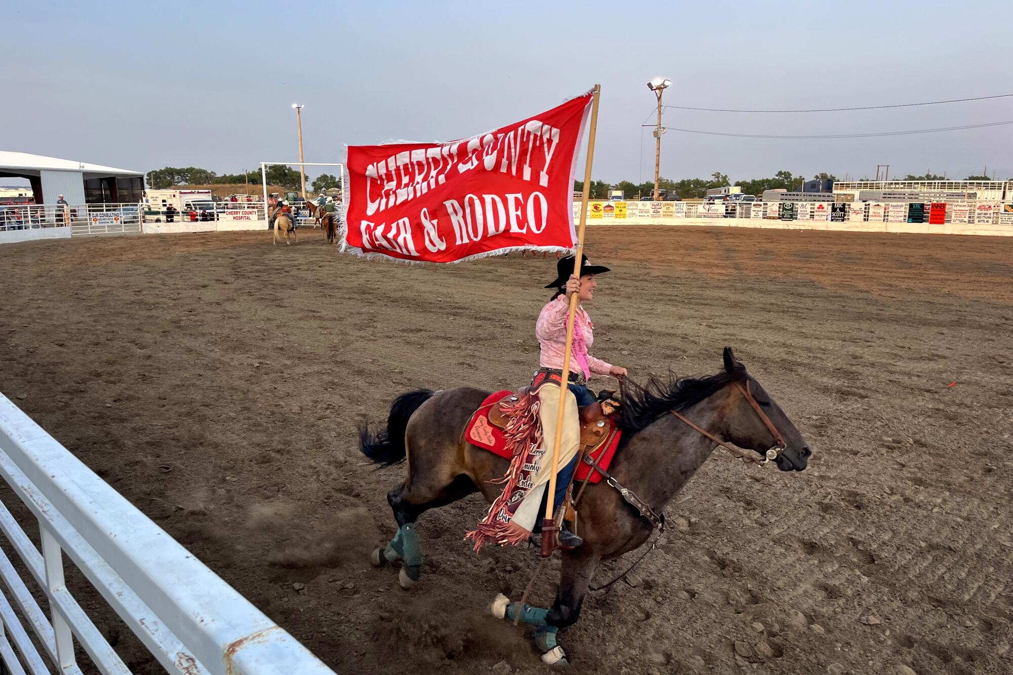 A woman rides a horse and carries a rodeo flag.