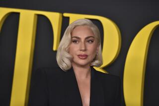 Lady Gaga with her hair styled in a short blond bob wears a black blazer 