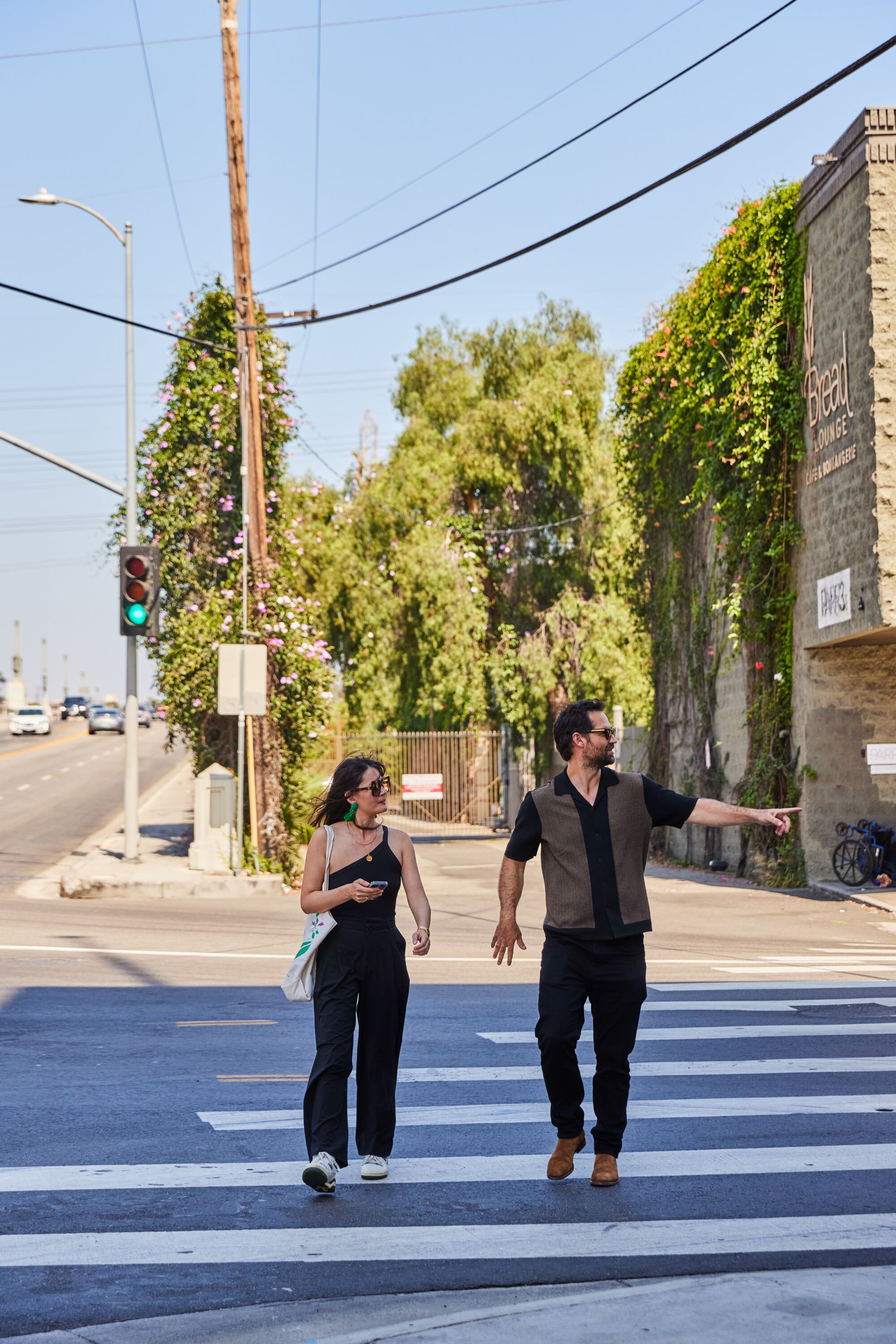 A woman with dark hair and a man with dark hair walk on a crosswalk.