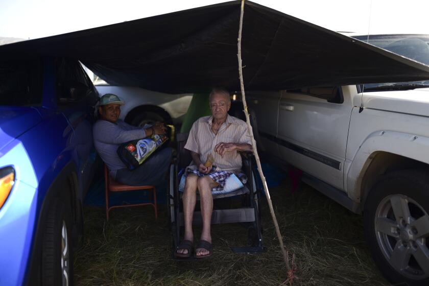 In this Friday, Jan. 10 photo, residents from the Indios neighborhood of Guayanilla, Puerto Rico, Milagros Figueroa and Ruben Fantausi, sit under a tarp between vehicles parked on a private hay farm where locals affected by earthquakes have set up shelter amid aftershocks in Guayanilla, Puerto Rico. A 6.4 magnitude quake that toppled or damaged hundreds of homes in southwestern Puerto Rico is raising concerns about where displaced families will live, while the island still struggles to rebuild from Hurricane Maria two years ago. (AP Photo/Carlos Giusti)