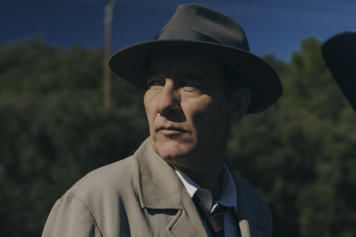 A man outside in trench coat and hat stares to the side suspiciously in "Monsieur Spade."