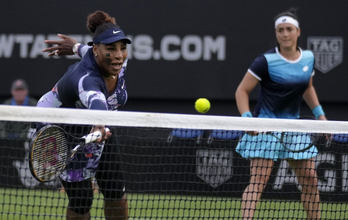 Serena Williams returns the ball as Ons Jabeur of Tunisia looks on.