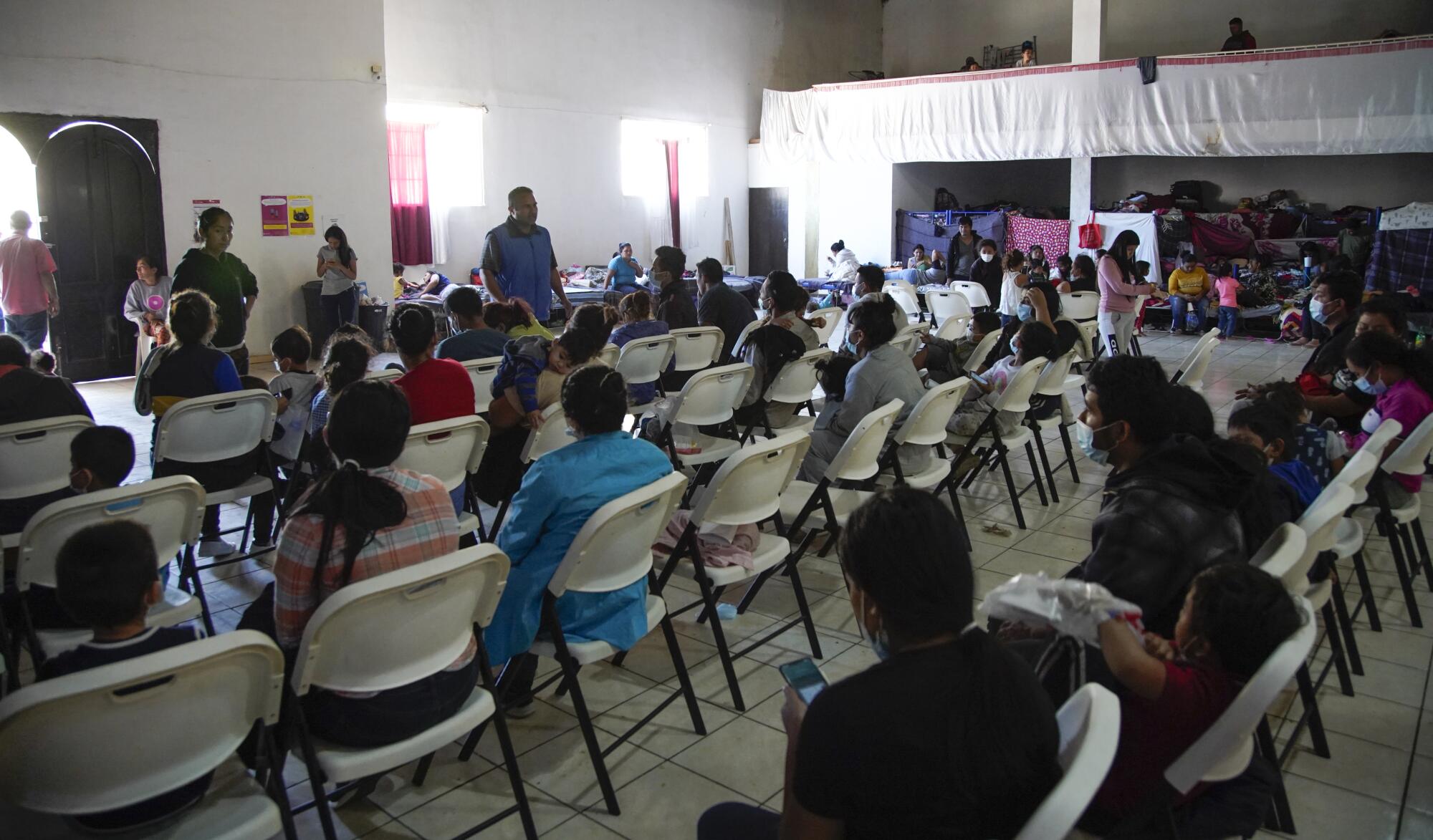 Asylum seekers seated in rows of chairs at Tijuana shelter