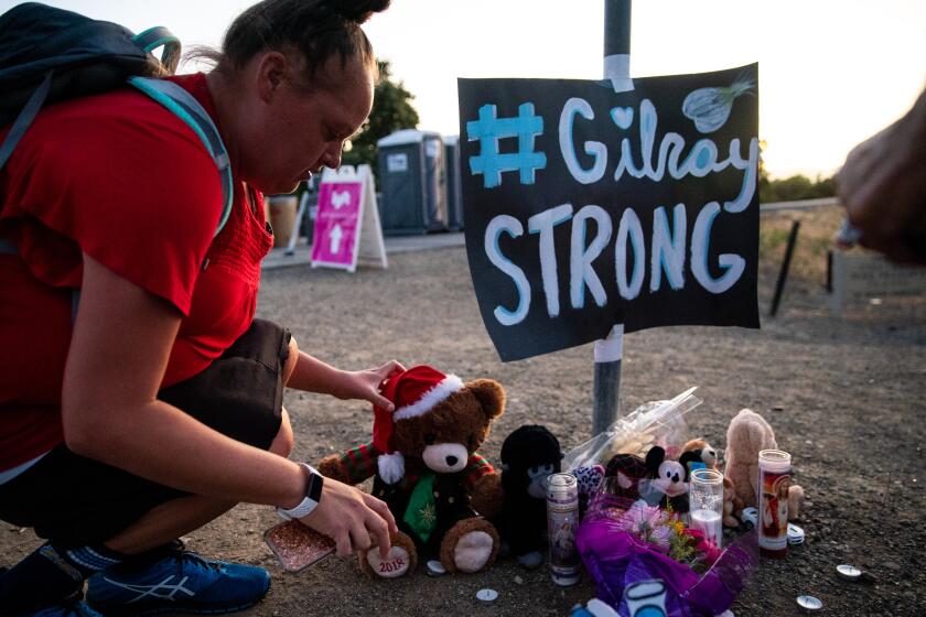 GILROY, CALIF. - JULY 30: Laura Miller places a stuff bear at a memorial, to those that lost their lives in the mass shooting at the Gilroy Garlic Festival, sits on the roadside, at the intersection of Uvas Parkway and Miller Avenue on Tuesday, July 30, 2019 in Gilroy, Calif. (Kent Nishimura / Los Angeles Times)