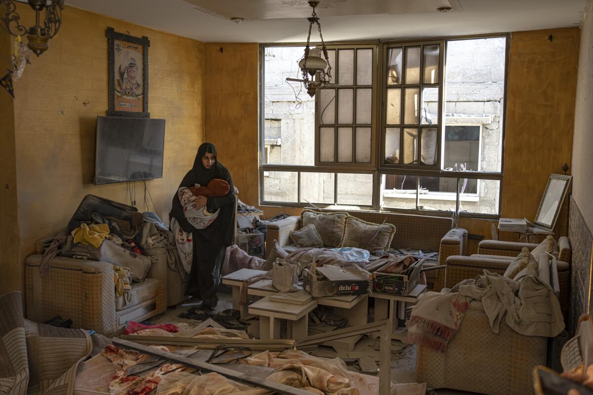 A Palestinian woman holds her child in a debris-filled room after an Israeli strike damaged her home