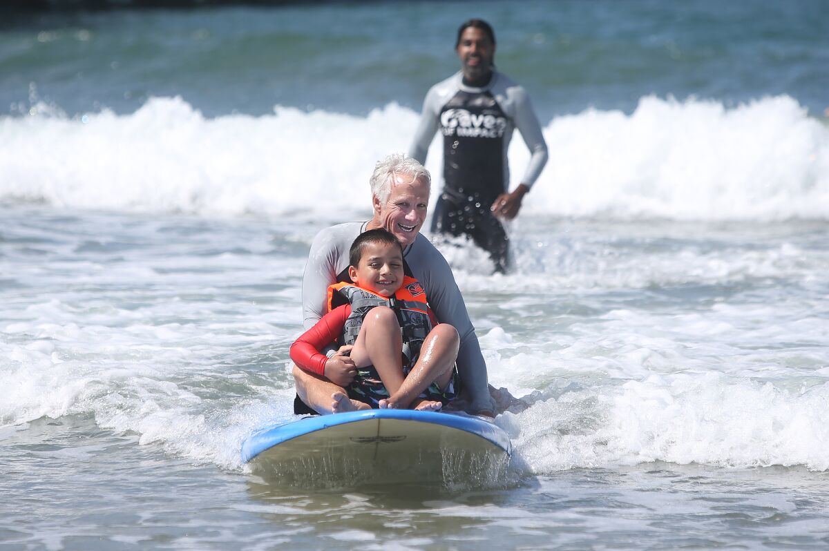 Instructor Tom Swanecamp catches a wave with a participant in the Miracles for Kids surf camp Friday at the Newport Pier in Newport Beach.