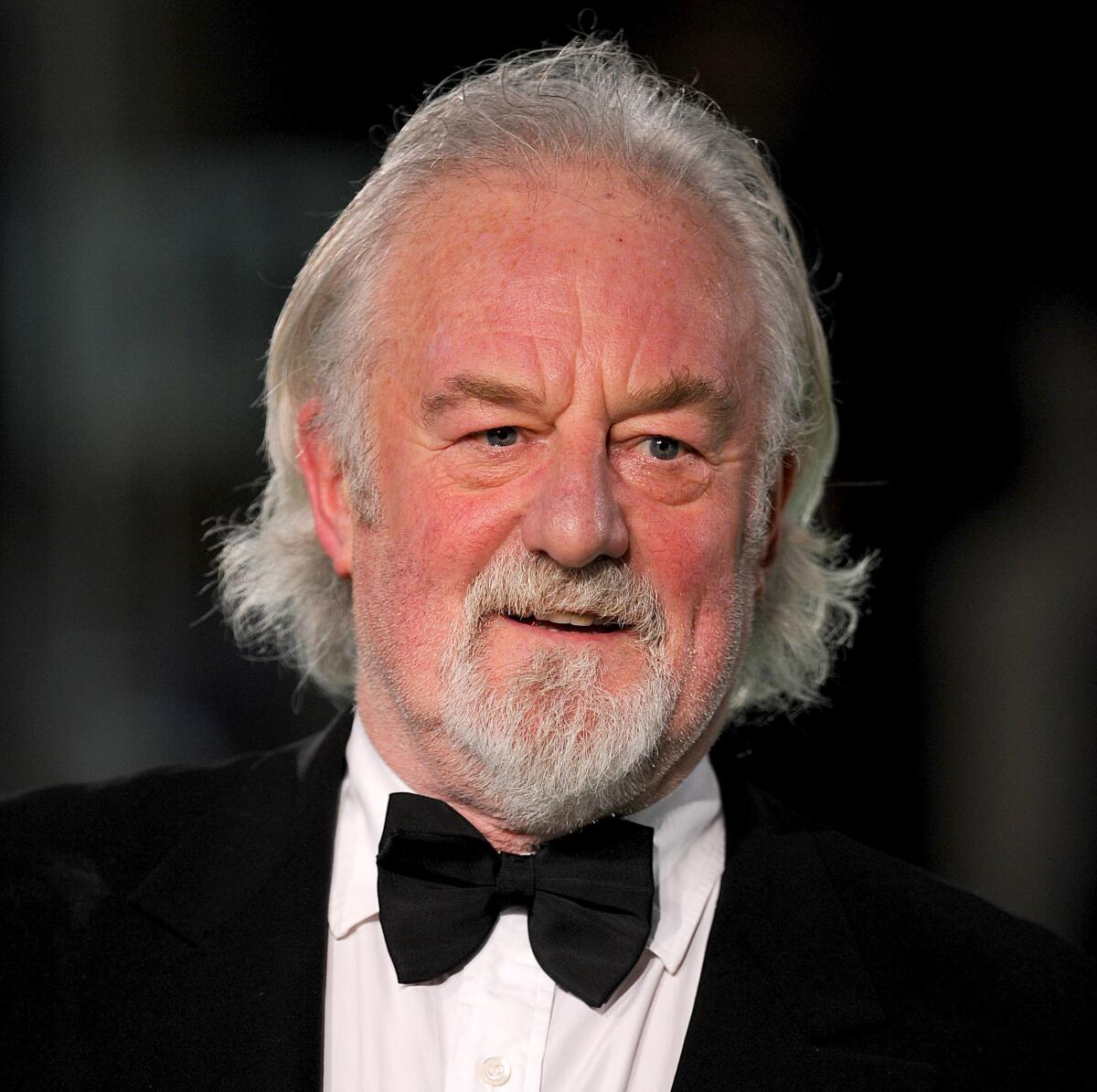 A smiling older man with gray hair, a gray beard and formal wear at a film premiere.