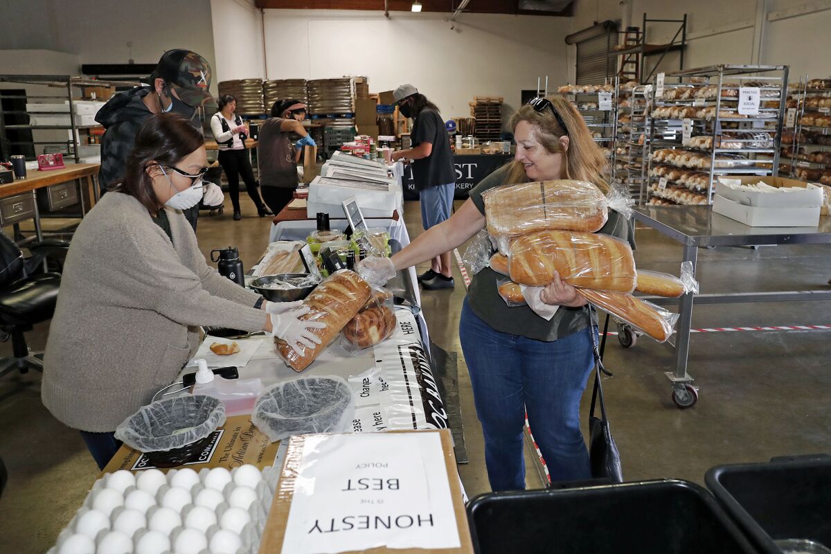 Claudia Klein, right, of Orange hands Sandy Nieva loaves of bread she's buying at a pop-up market at the OC Baking Co. warehouse in Orange. Klein did a shopping run for family members and a few friends.