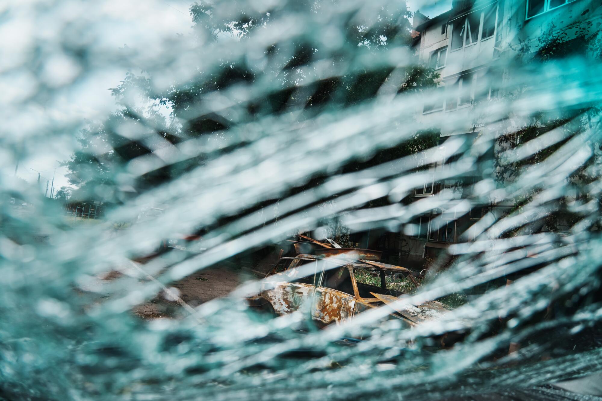 The splintered windshield of one car frames the view of a burned-out shell of another in Slovyansk, Ukraine