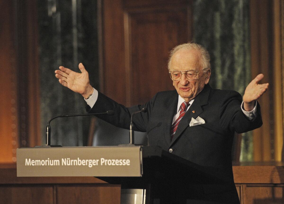 Benjamin Ferencz stands at a lectern and holds his hands out.