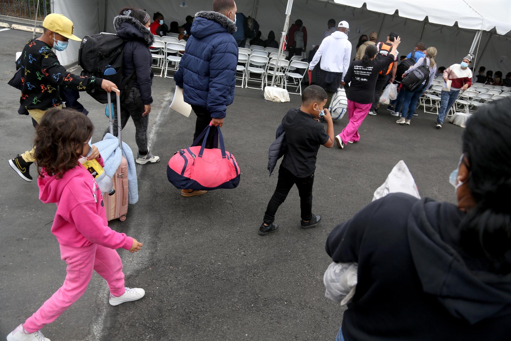 Os migrantes chegam de ônibus carregando seus pertences para o abrigo de migrantes da SDRRN