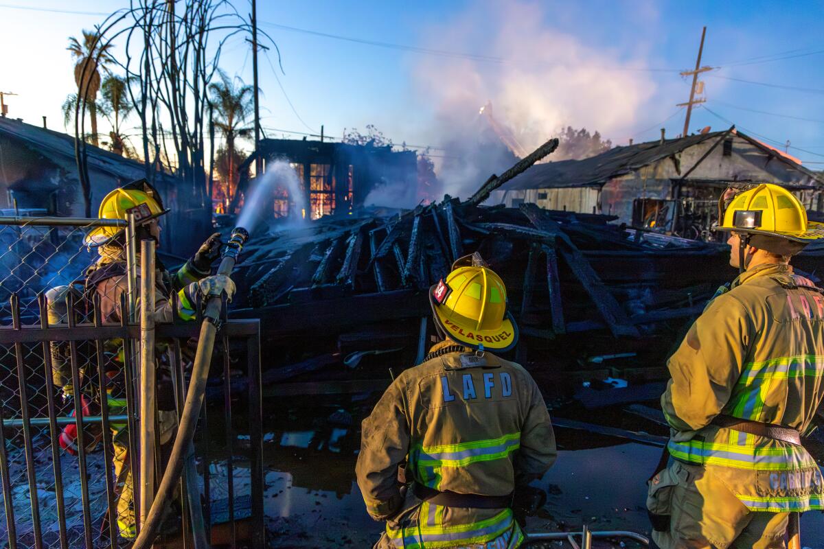Firefighters spray water on a smoldering pile of timber from a collapsed construction framing