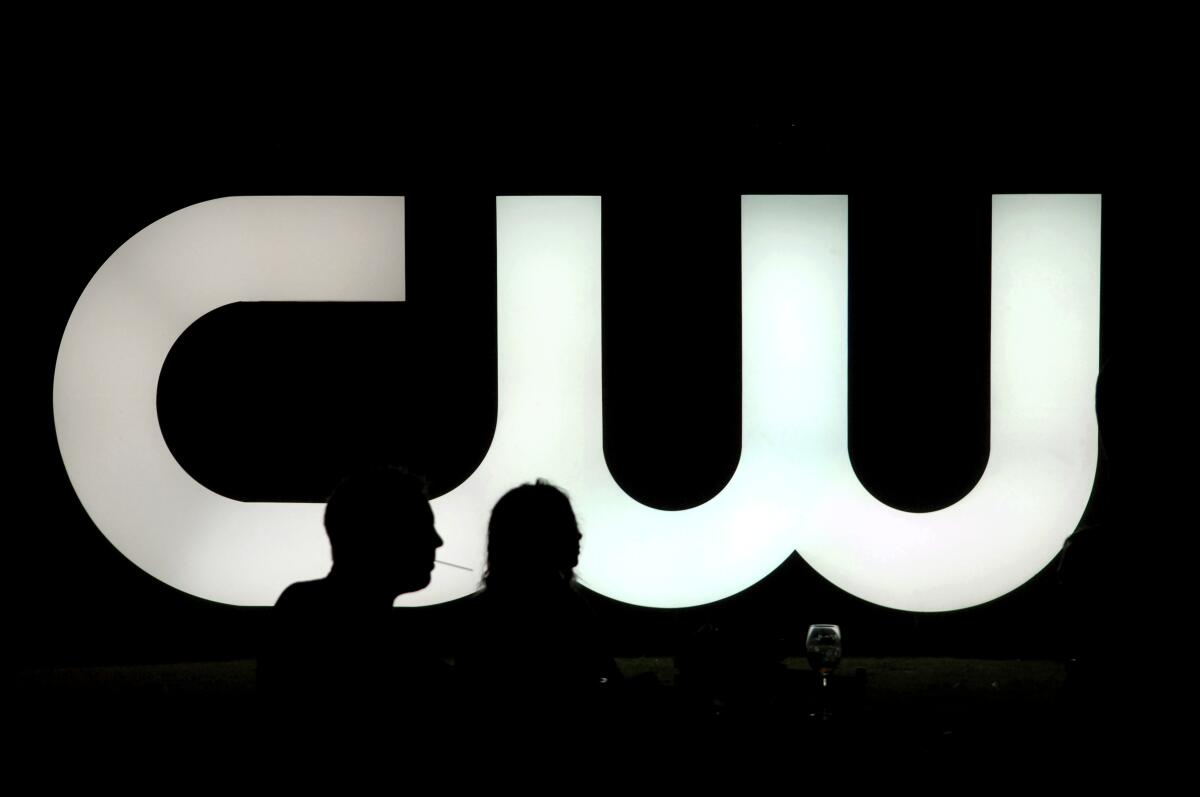 Silhouettes of two people in front of a large, lighted sign of the CW logo